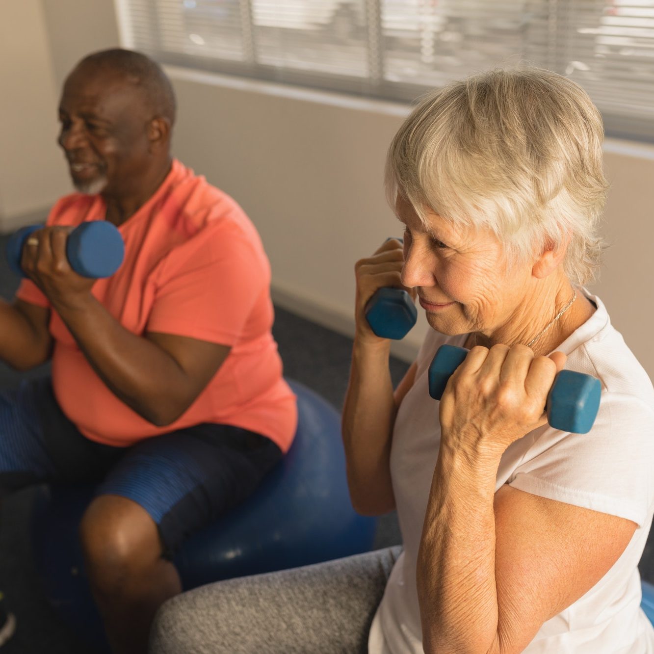 Side view of active senior people exercising with dumbbells at home