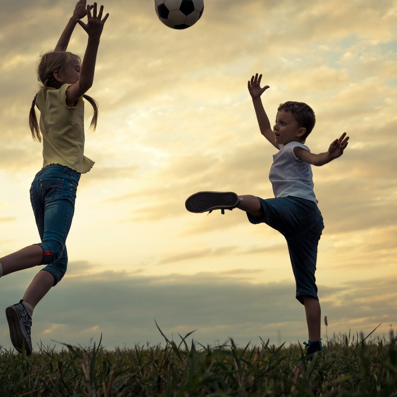 Happy young little boy and girl playing in the field with socce