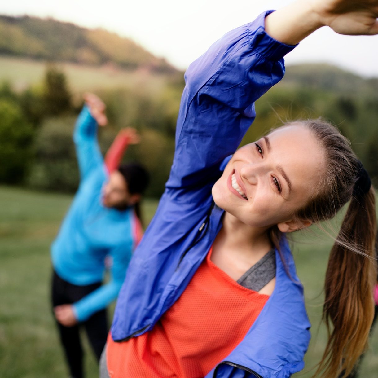 Large group of fit and active people doing exercise in nature, stretching.